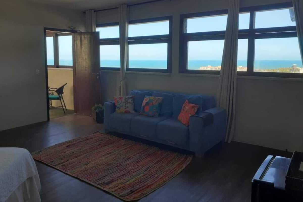 A room with a blue sofa, a patterned rug, and large windows offering a view of the sea.