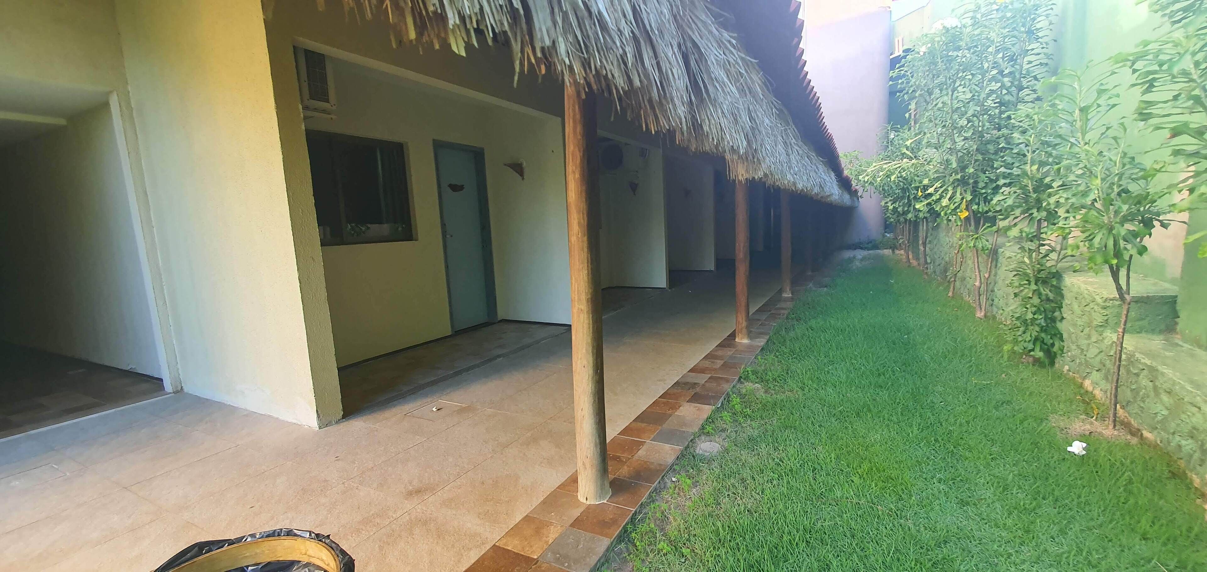 A covered outdoor area with a tiled floor, a thatched roof, and a small grassy area with plants.