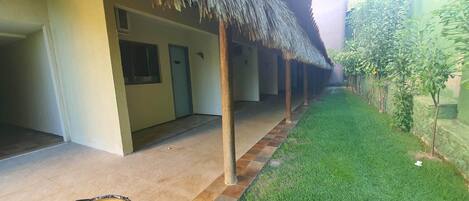A covered outdoor area with a tiled floor, a thatched roof, and a small grassy area with plants.