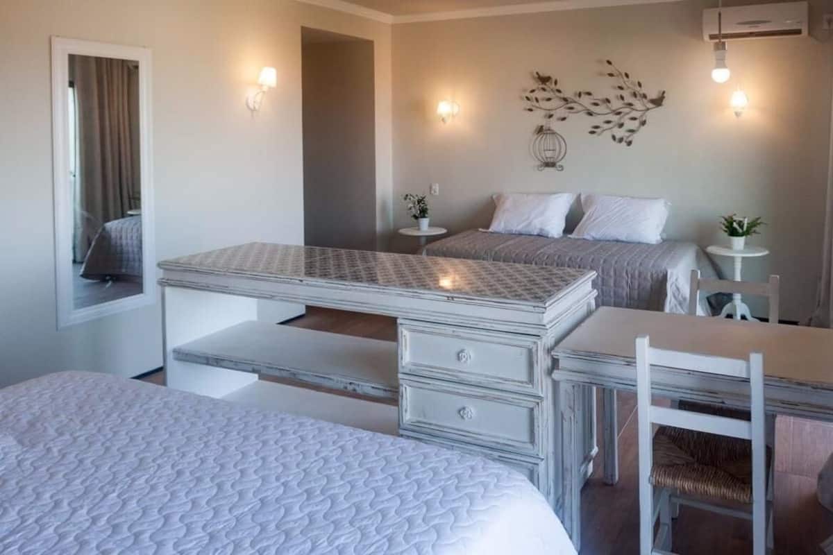 A bedroom with two beds, a desk, and a chair. There are wall-mounted lights and a decorative wall piece.