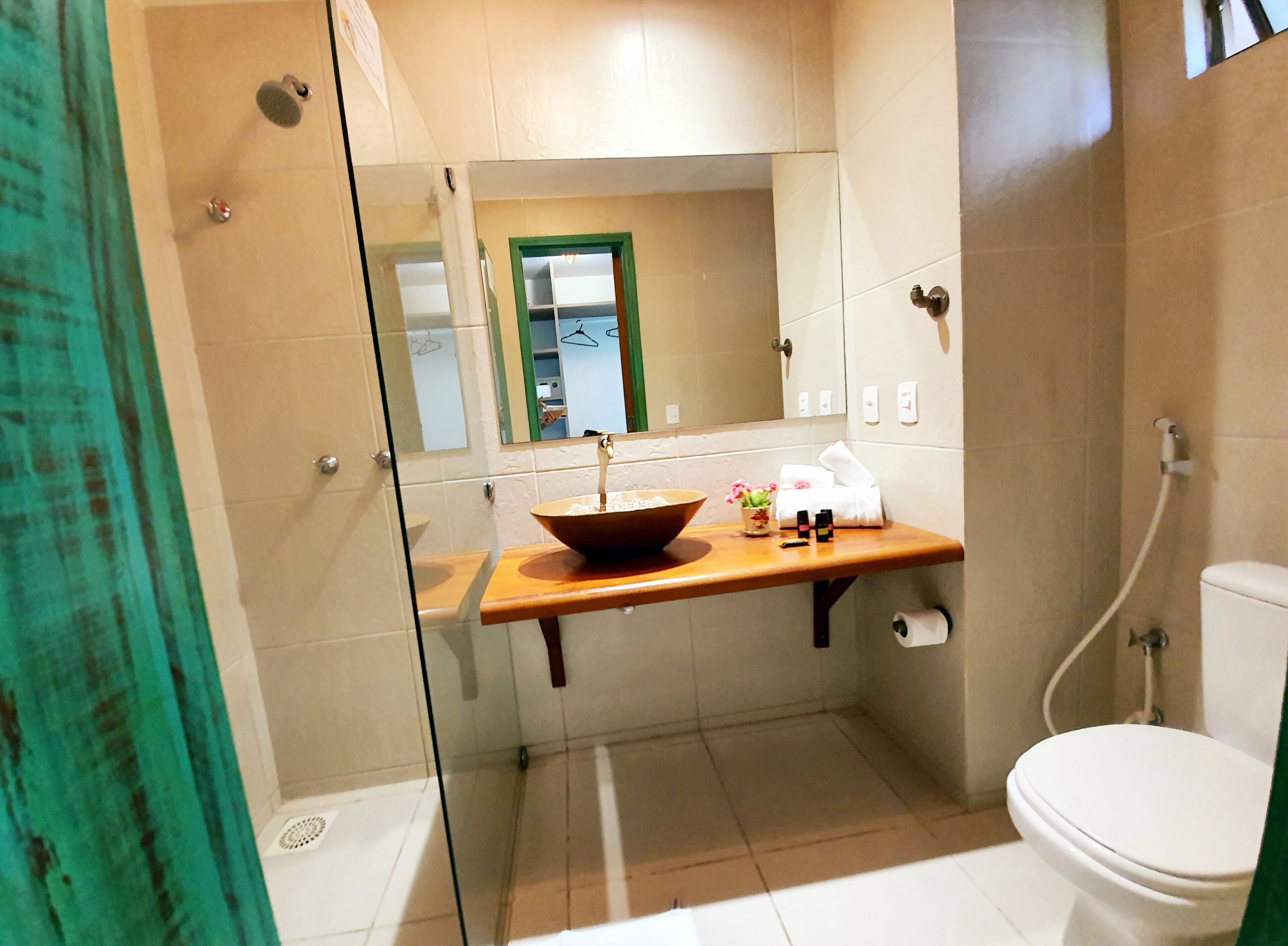 A modern bathroom with a glass shower enclosure, a wooden vanity with a bowl sink, a mirror, and a toilet.