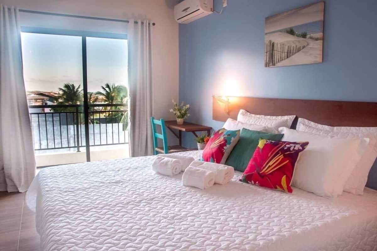 A hotel room with a large bed, a view of the sea, a balcony, and a painting on the wall.