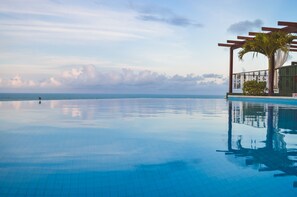 Piscina azul cristalina con una pérgola de madera y una palmera, con vistas al océano.
