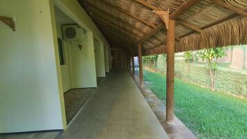 Un corredor cubierto con suelo de baldosas, techo de paja y zona ajardinada con árboles.