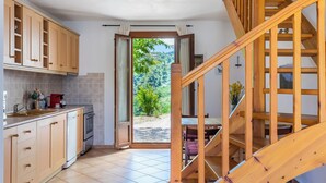 Eine Küche mit Holzausstattung, einem Geschirrspüler und einem Backofen. Eine Holztreppe führt zu einem Balkon mit Blick ins Grüne.