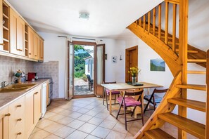 Eine Küche mit Holzausstattung, einem Esstisch und Stühlen. Eine Holztreppe führt zu einer weiteren Ebene.