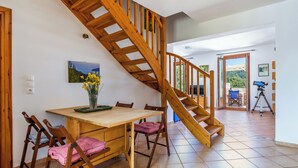 Eine Holztreppe führt zu einem Balkon, ein Essbereich mit Tisch und Stühlen sowie ein Teleskop auf einem Stativ.