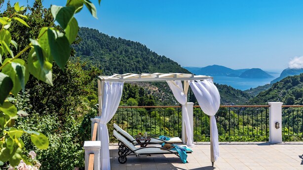Ein sonniger Außenbereich zum Entspannen mit einer Pergola, einer Liege und Blick auf eine gebirgige Landschaft.