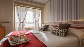 Une chambre d’hôtel avec un grand lit, deux oreillers, un plateau avec une tasse et des toasts, et une fenêtre avec des rideaux.
