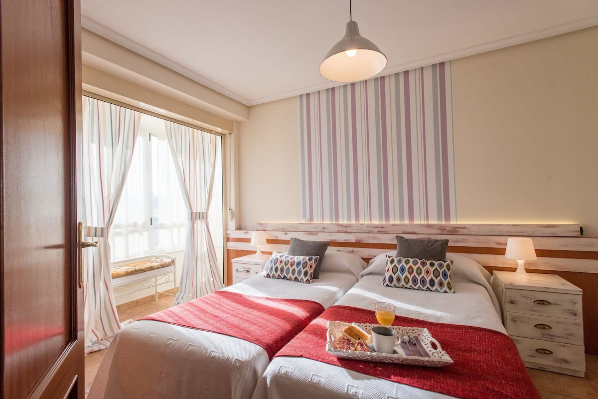 A hotel room with two beds, a breakfast tray, and a large window with curtains.