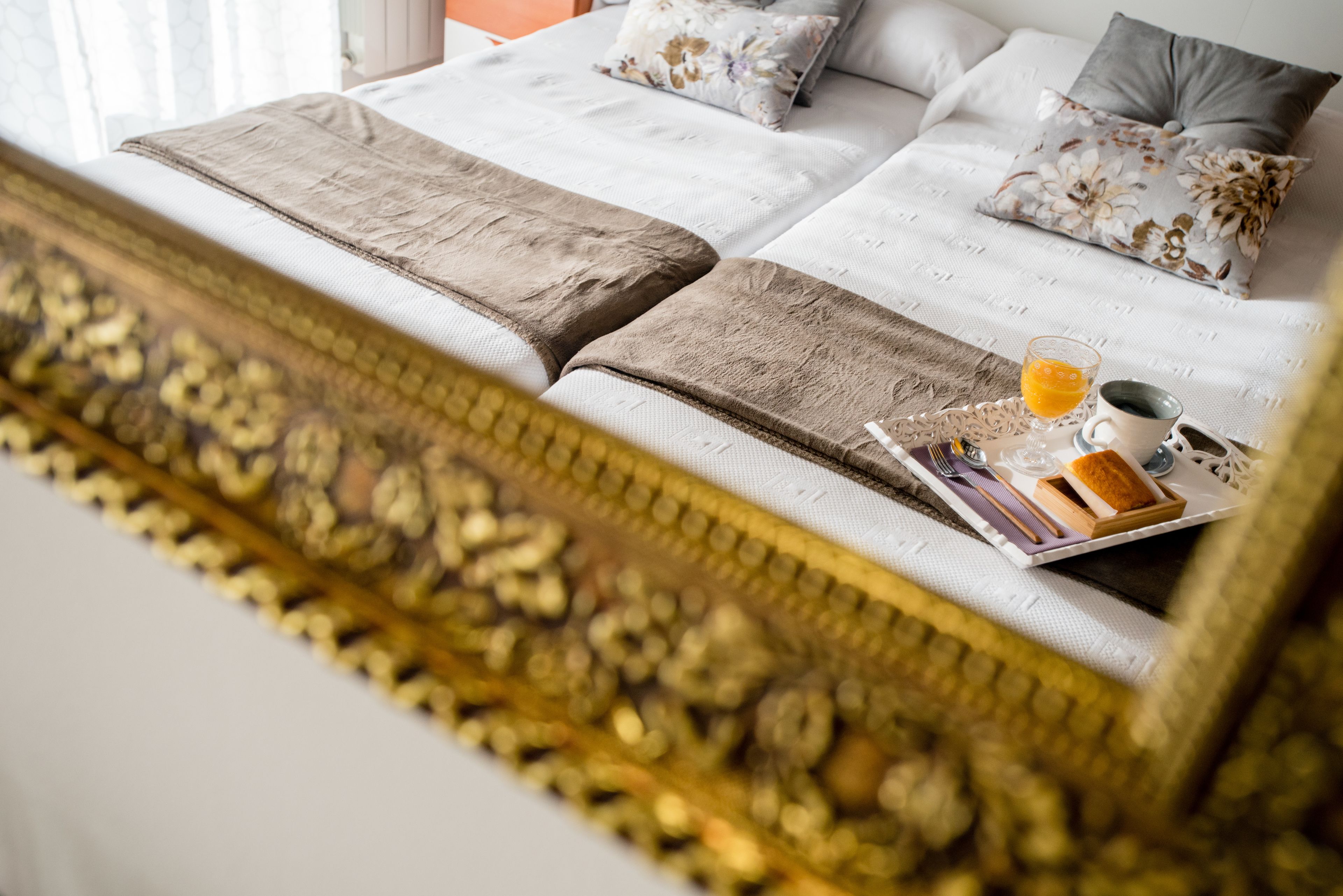 Una cama bien hecha con una bandeja de desayuno que incluye jugo de naranja y tostadas, en una habitación de hotel.