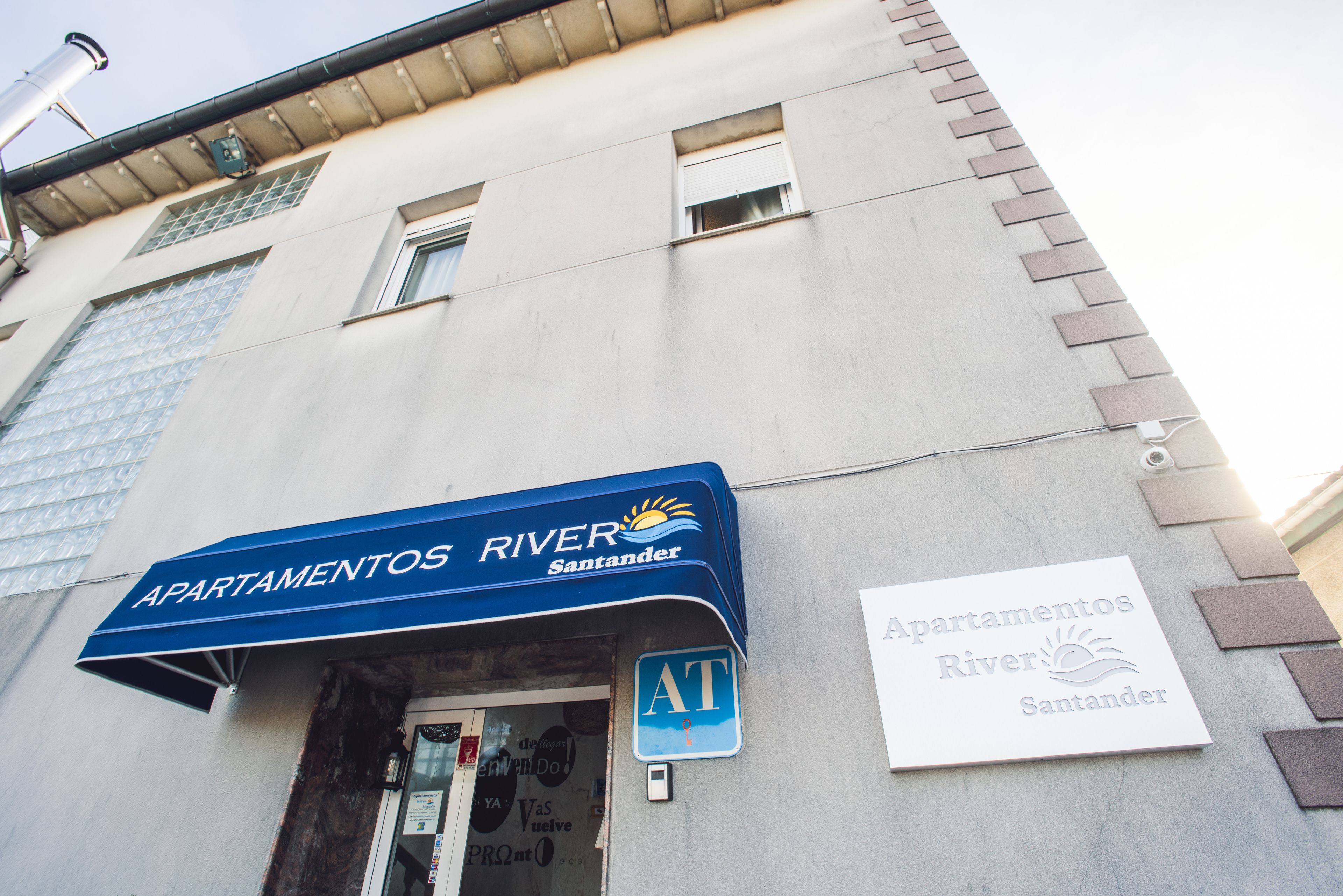 Un edificio con un cartel que dice 'Apartamentos River Santander' y un toldo azul.