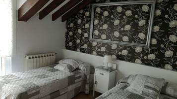 A bedroom with two beds, a nightstand, a radiator, and a floral wallpaper.