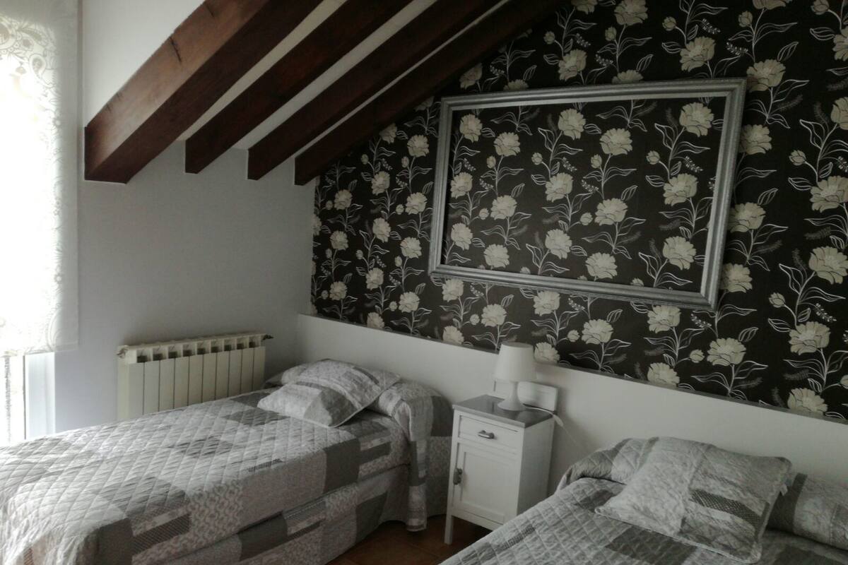 A bedroom with two beds, a nightstand, a radiator, and a floral wallpaper.