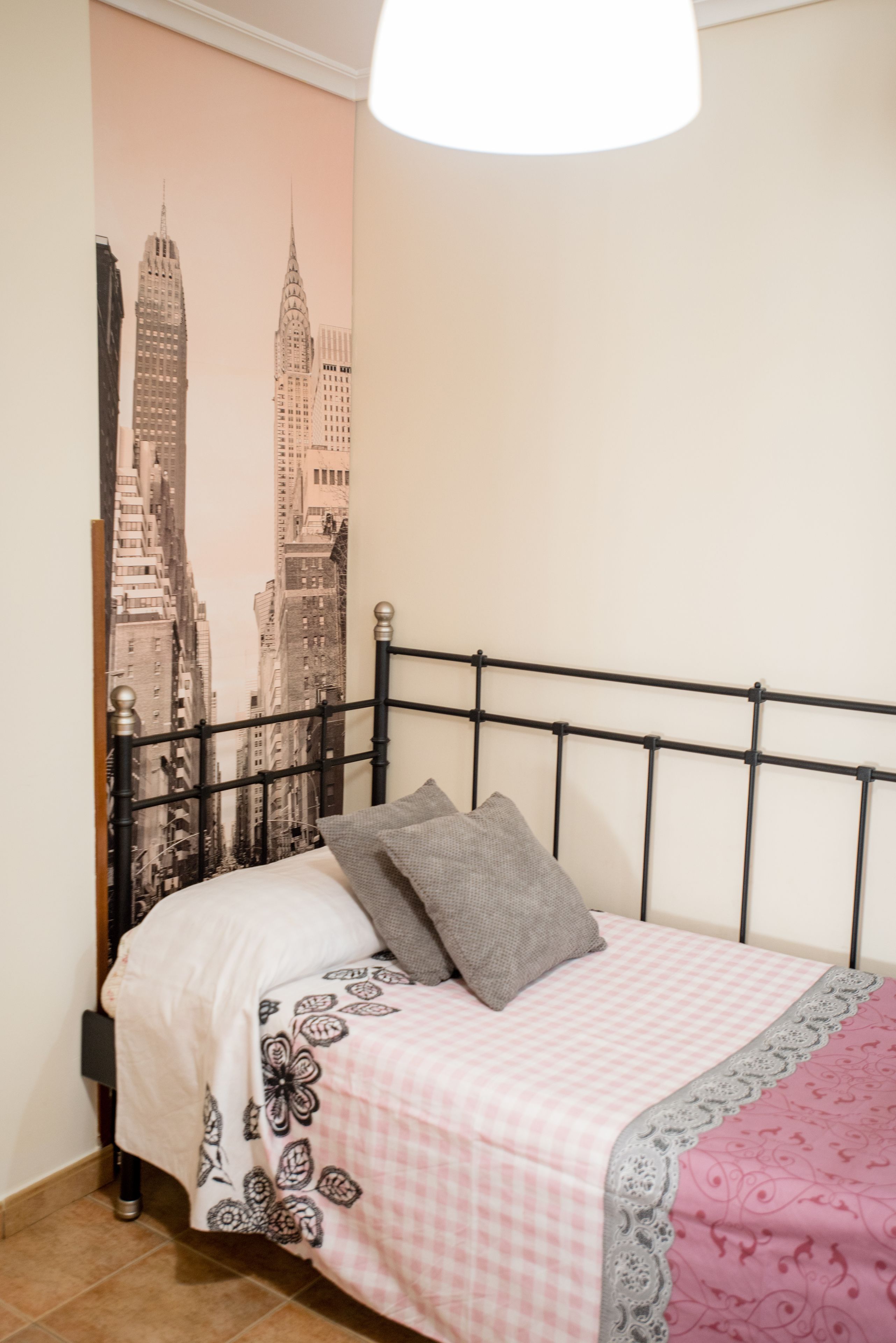 A bedroom with a bed, pillows, a headboard, and a wall with a cityscape poster.
