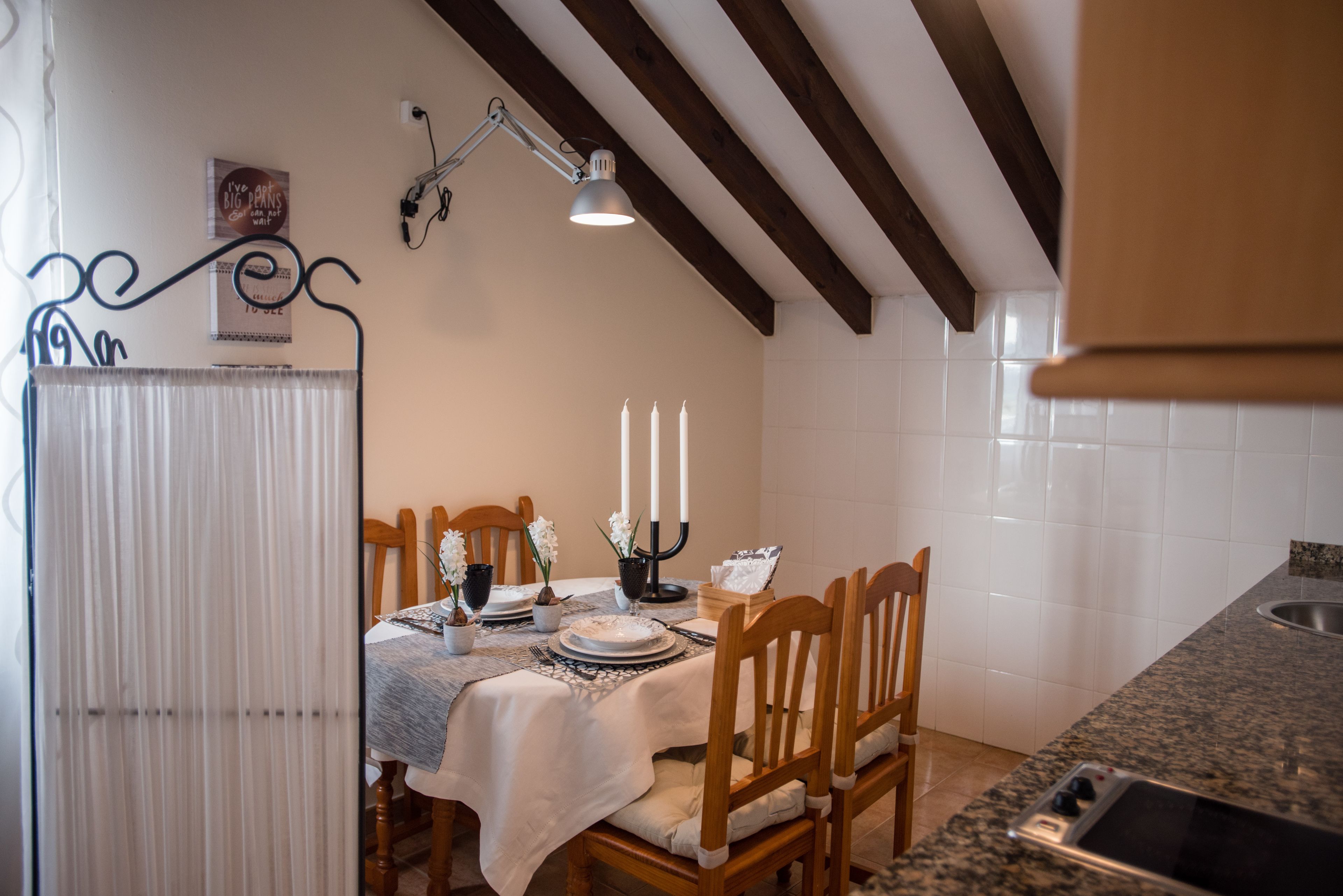 A dining area with a table set for four, wooden chairs, a candle holder, and a wall-mounted lamp.