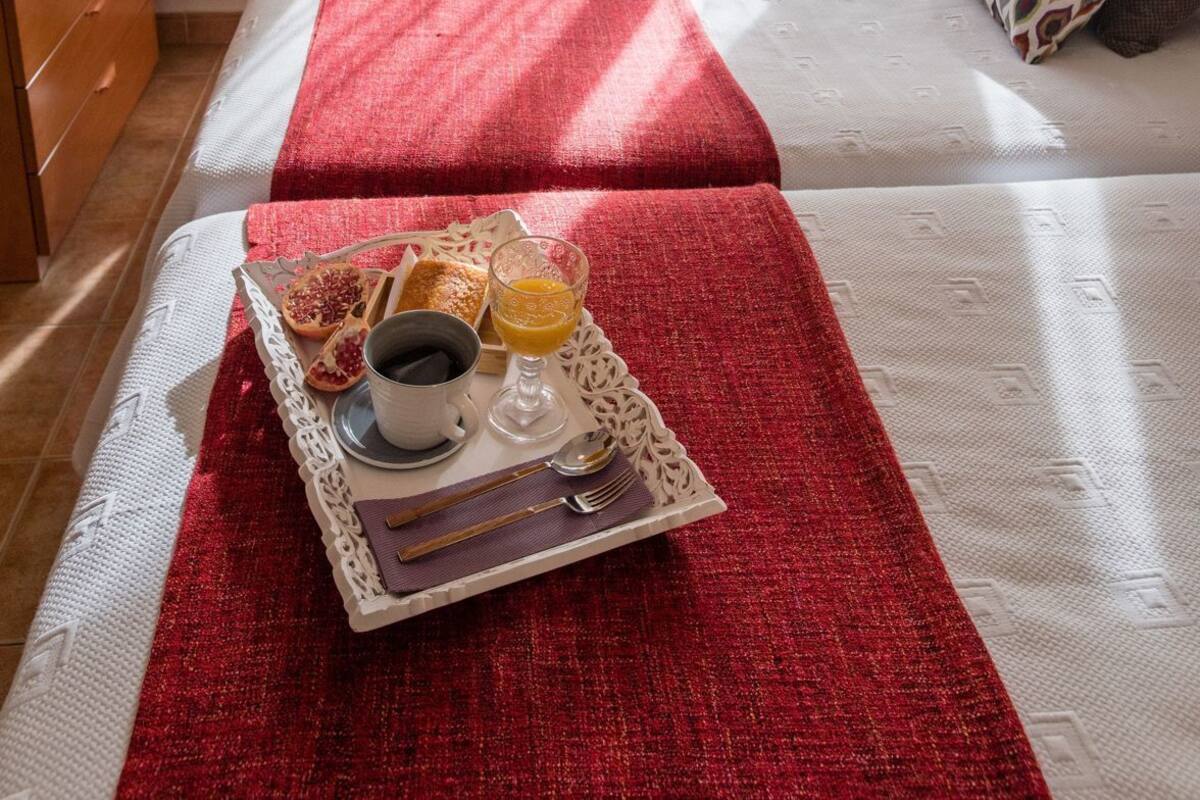 A bedroom with a bed, a bedside table, a window with curtains, and a tray with breakfast items.
