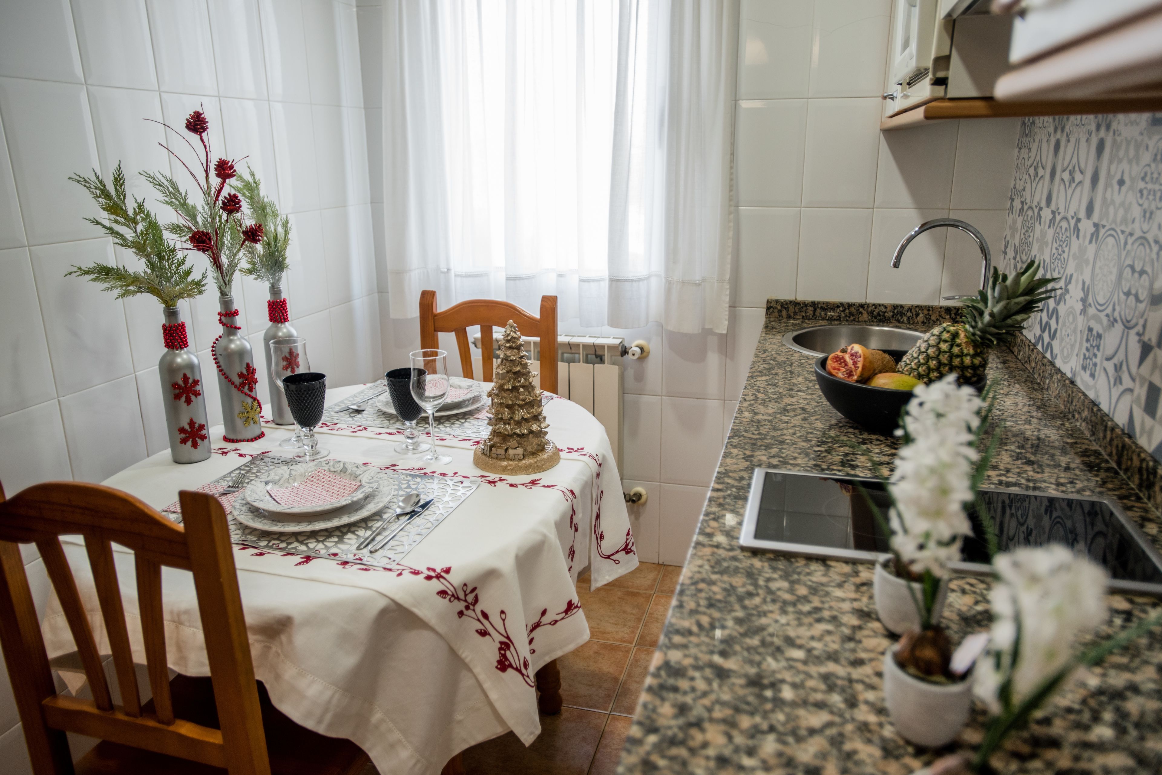 Un comedor con una mesa dispuesta para dos, un árbol de Navidad y un frutero en la encimera.