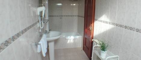 A bathroom with a toilet, bidet, sink, and shower. There is a towel rack and a small shelf with a plant.
