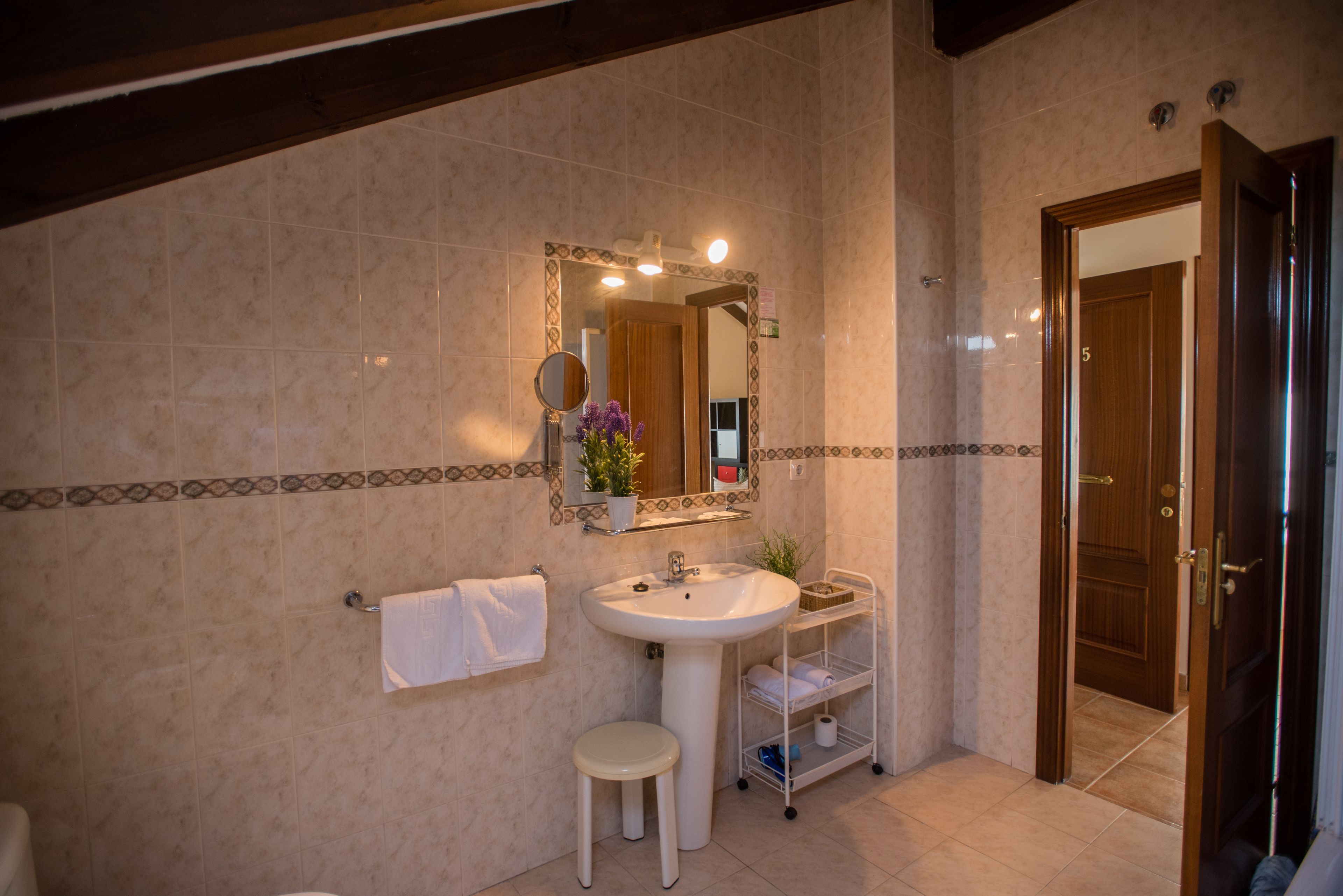 A bathroom with a sink, mirror, towel rack, and a small stool.