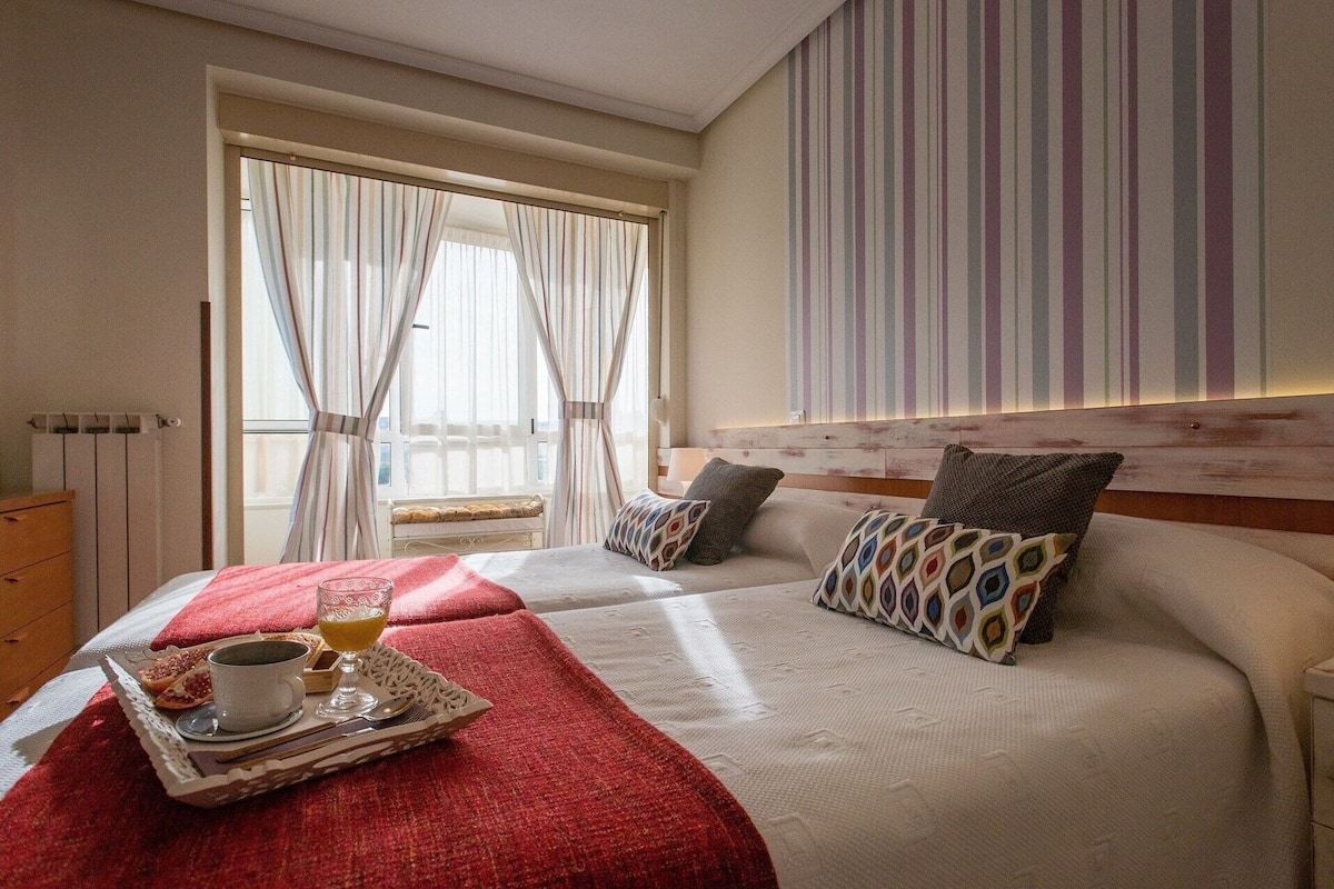 A hotel room with a bed, a window with curtains, a radiator, and a wall with a striped pattern.