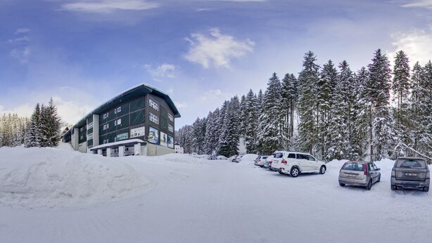 A hotel with multiple floors, a parking area with several cars, and a snowy forest in the background. - SkiHotel Lenka (Spindleruv Mlyn)