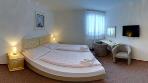 A hotel room with a curved bed, bedside lamps, a desk, a chair, a television, and a window with curtains. - SkiHotel Lenka (Spindleruv Mlyn)