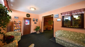 A lobby with a reception desk, a bookshelf, two patterned sofas, a potted plant, and a wall-mounted wreath. - SkiHotel Lenka (Spindleruv Mlyn)