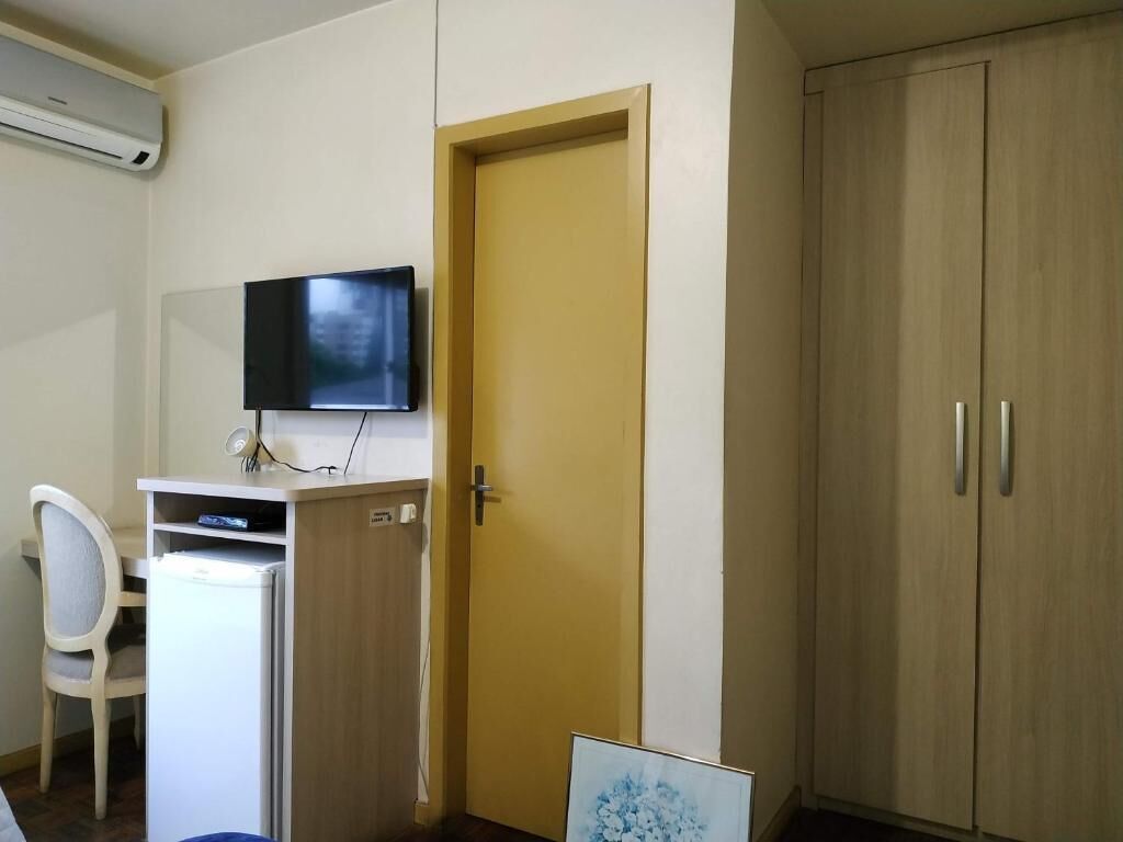 Een kamer met een bureau, stoel, televisie, kledingkast en een deur.