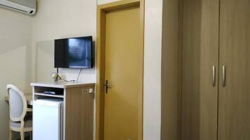 Een kamer met een bureau, stoel, televisie, kledingkast en een deur.