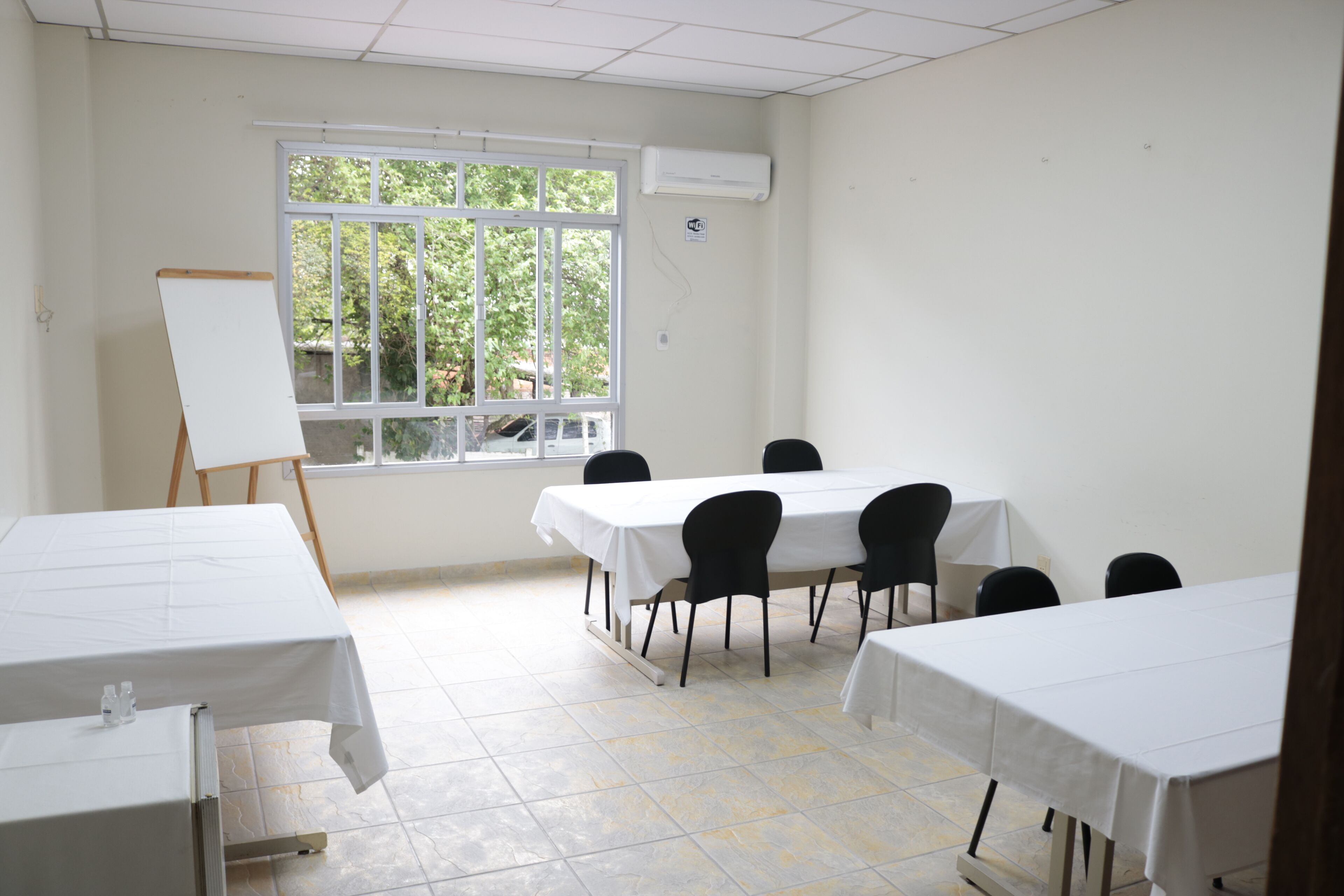 A conference room with a large window, white tables, and black chairs.