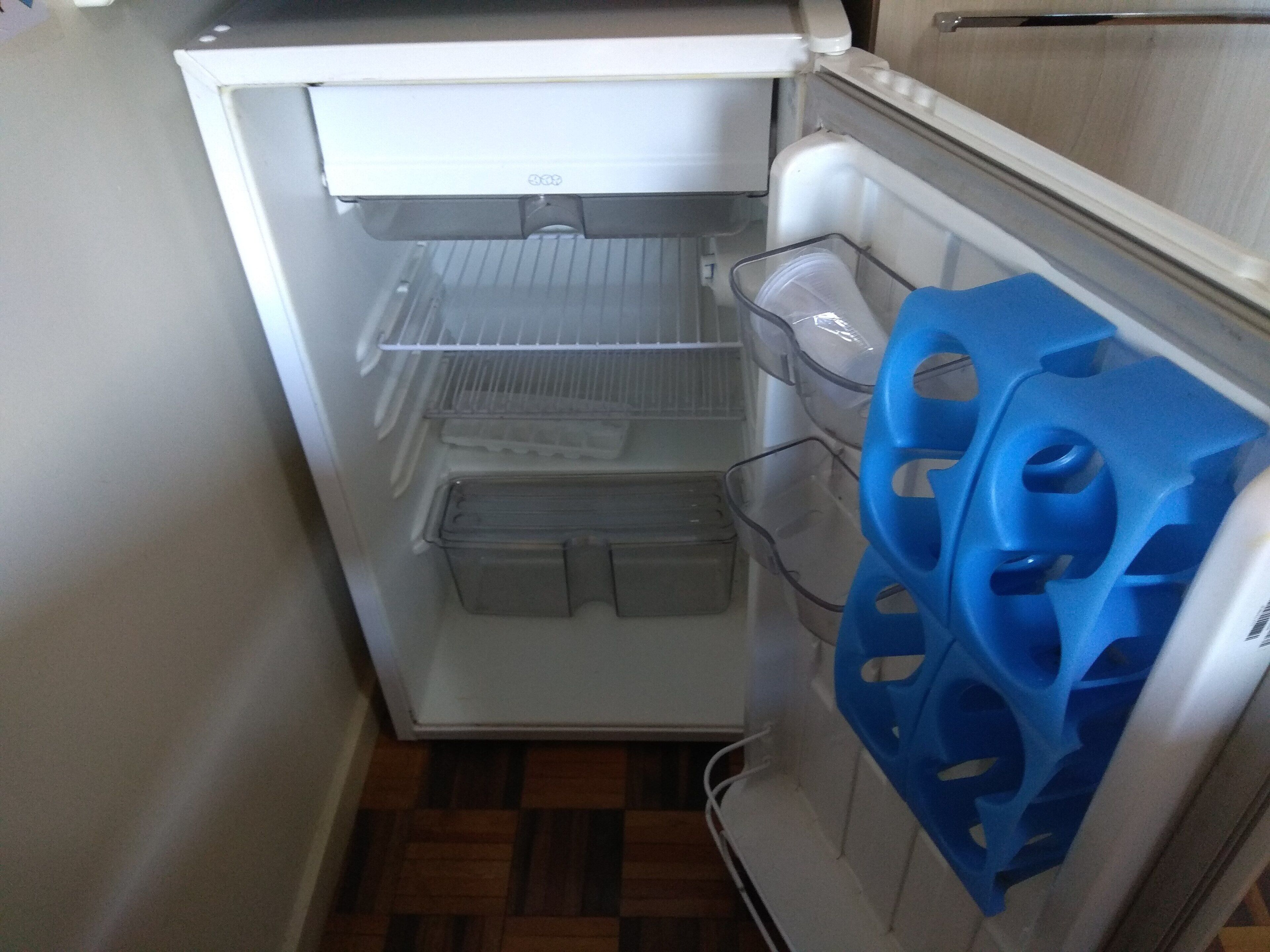 Ein kompakter Kühlschrank mit mehreren Ablagen und einem Gefrierfach, eingebaut in einer kleinen Küchenzeile mit Holzboden.