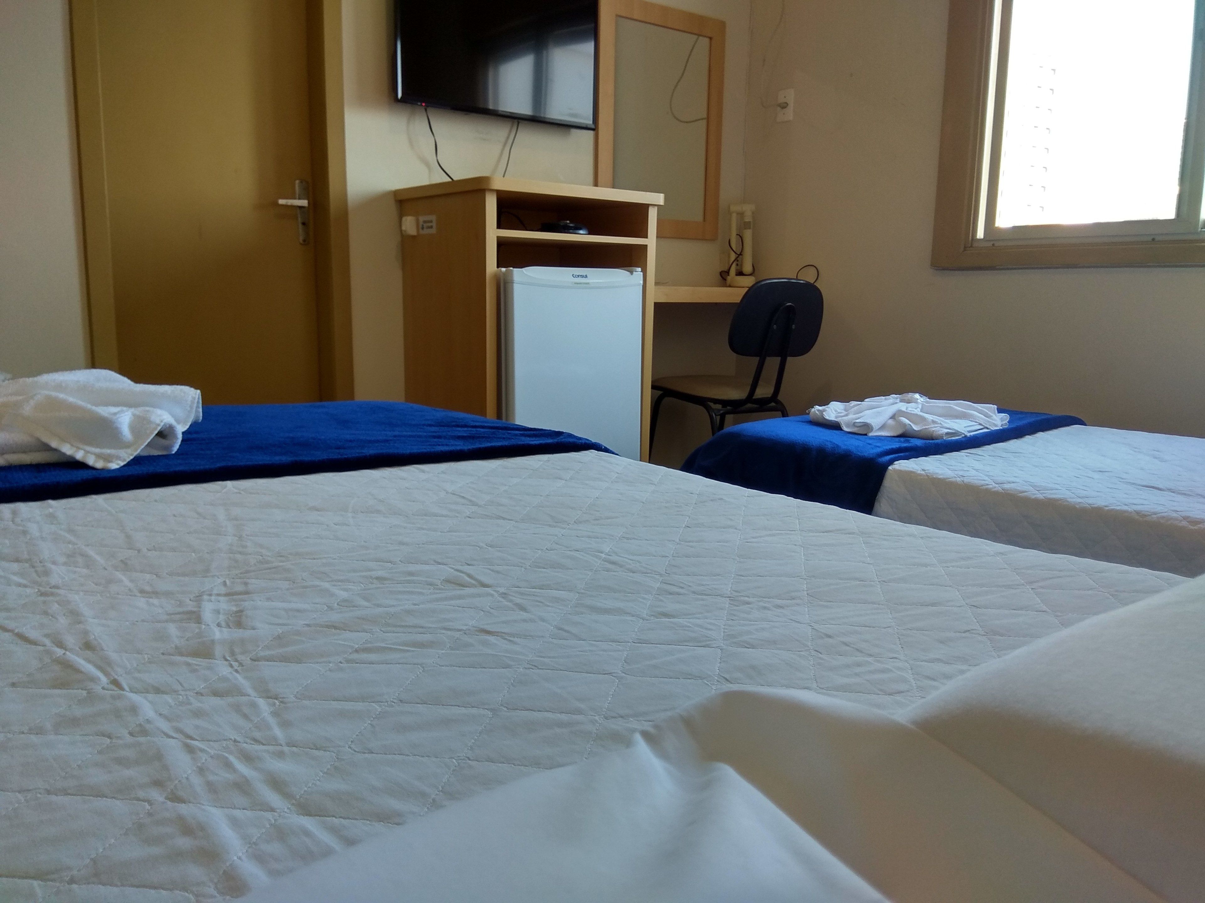 Habitación de hotel con dos camas, un escritorio, una silla, un televisor y una ventana.