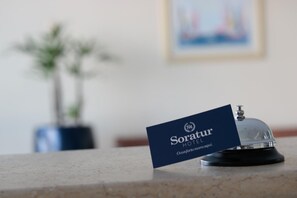 A hotel reception area with a sign that reads "Soratur HOTEL" and a bell. - Soratur Hotel & Coworking (Criciuma)