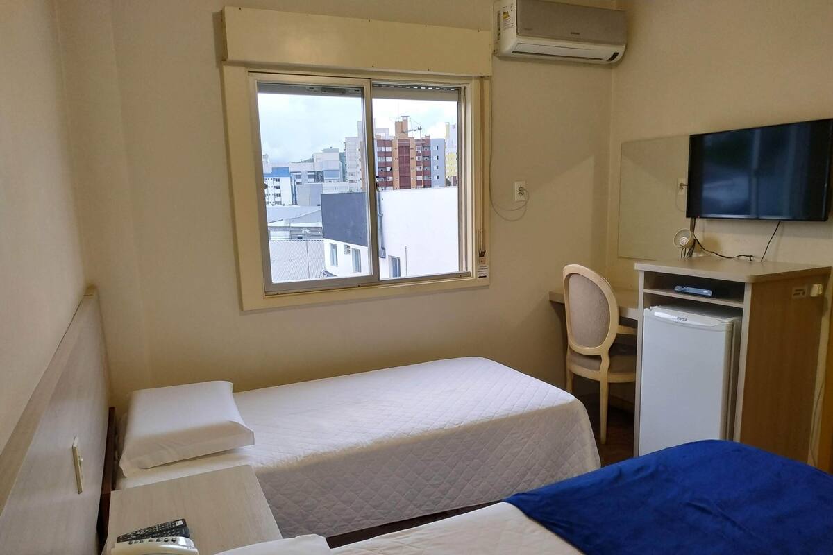 Una habitación de hotel con dos camas, un escritorio con una silla, un televisor y un refrigerador.