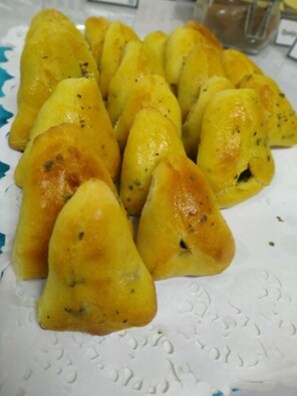 A plate of golden-brown triangular pastries with visible herbs on a white paper plate. - Soratur Hotel & Coworking (Criciuma)