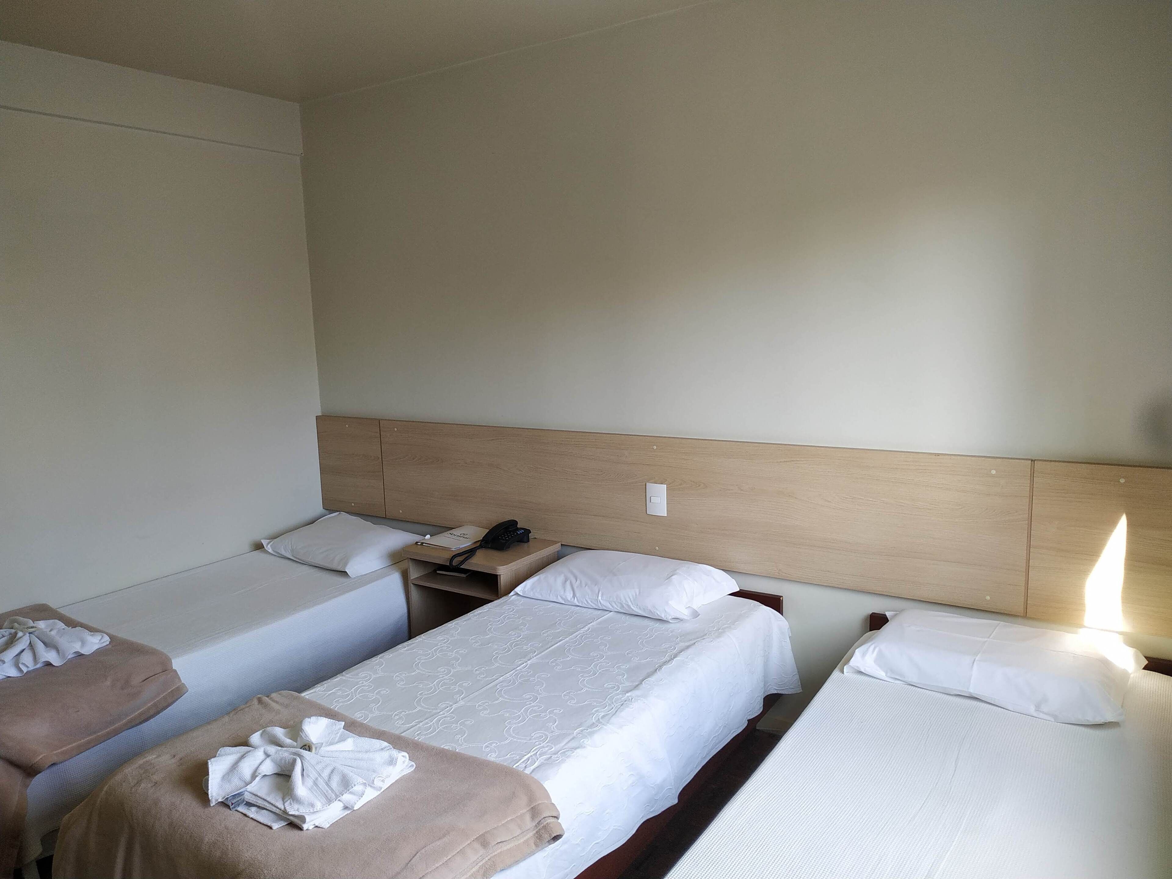 Una habitación de hotel con tres camas individuales, una mesita de noche con teléfono y una mesita auxiliar.