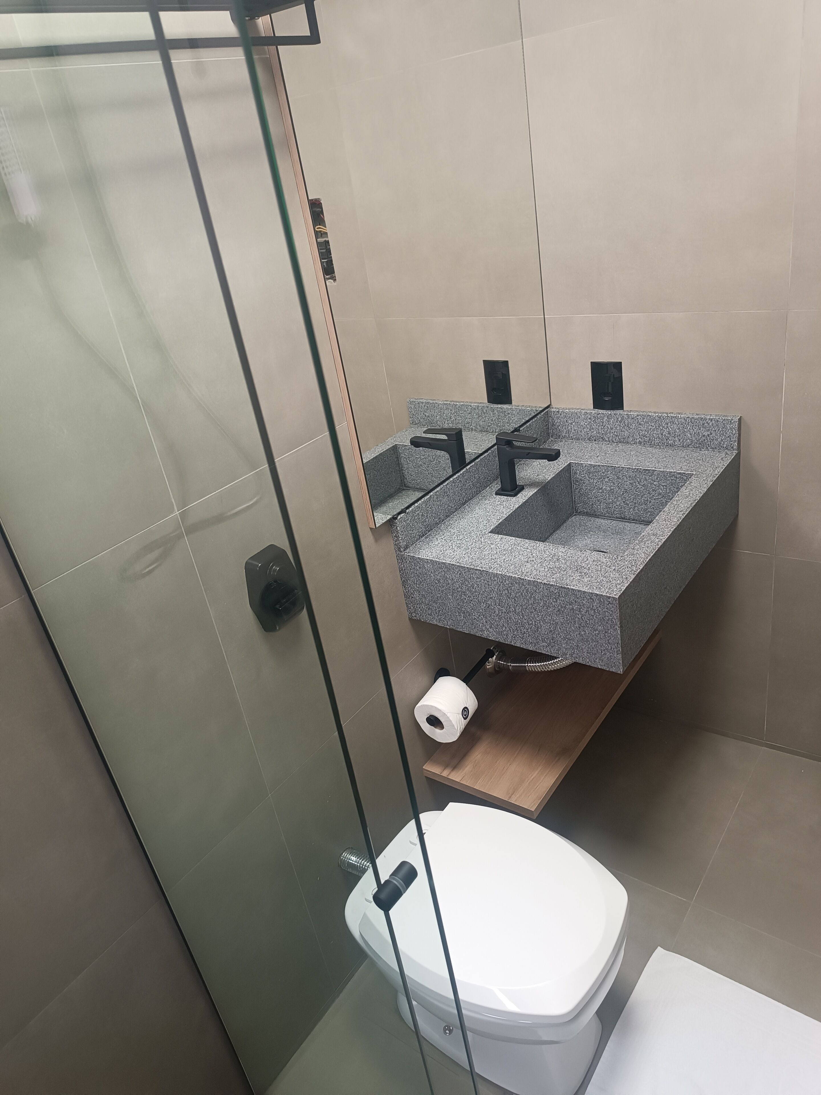 A modern bathroom with a glass shower enclosure, a white toilet, and a granite sink with a wooden shelf.