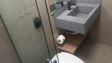 A modern bathroom with a glass shower enclosure, a white toilet, and a granite sink with a wooden shelf.