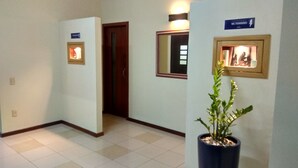 A hallway with a potted plant, a framed picture, and a sign indicating a women's restroom. - Soratur Hotel & Coworking (Criciuma)