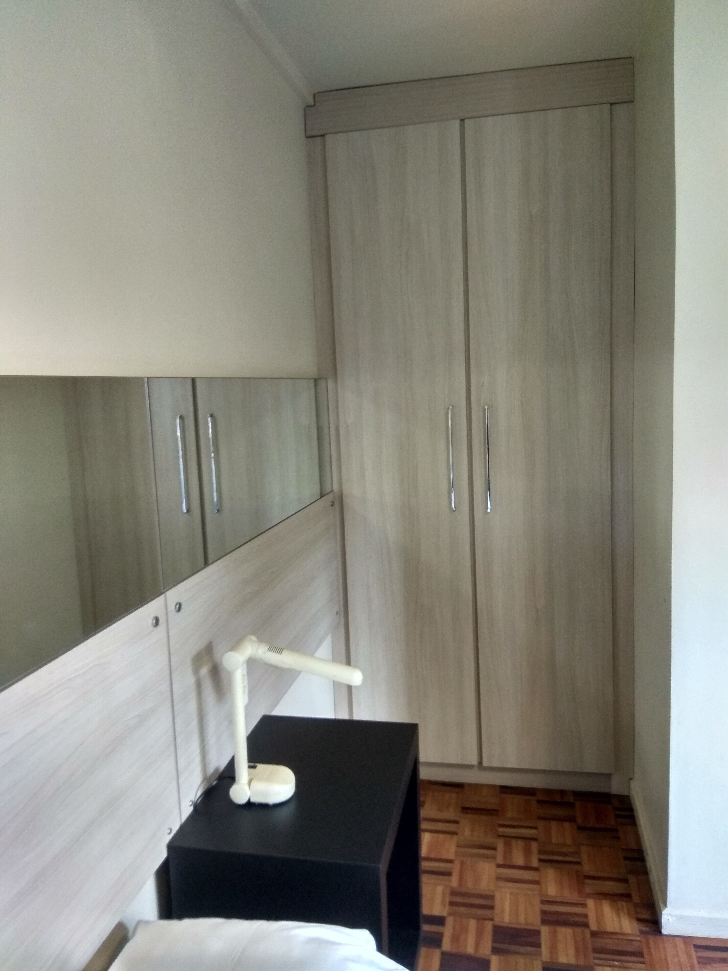 A bedroom with a bed, a bedside table with a lamp, and a wardrobe.