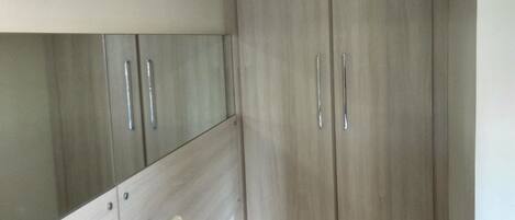 A bedroom with a bed, a bedside table with a lamp, and a wardrobe.