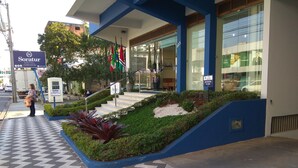 The entrance of Soratur Hotel with a staircase leading up to the entrance, surrounded by greenery and a patterned floor. - Soratur Hotel & Coworking (Criciuma)