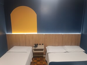 A hotel room with two beds, a wooden headboard, a small bedside table with a phone, and a wall-mounted light. - Soratur Hotel & Coworking (Criciuma)