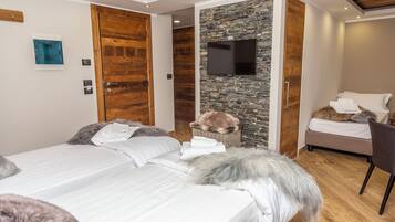 A modern hotel room with a wooden ceiling, a stone accent wall, a flat-screen TV, a bed with white linens, a small wicker basket, and a chair.