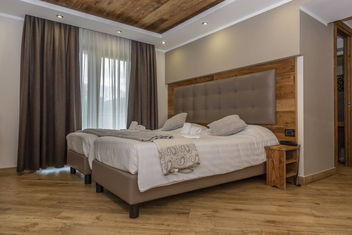 Un lit double avec une tête de lit en bois, une table de chevet avec un téléphone et une grande fenêtre avec des rideaux.