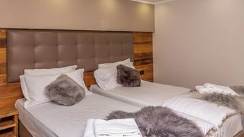Quarto de hotel com duas camas, cabeceira de madeira, roupa de cama branca e almofada fofa.