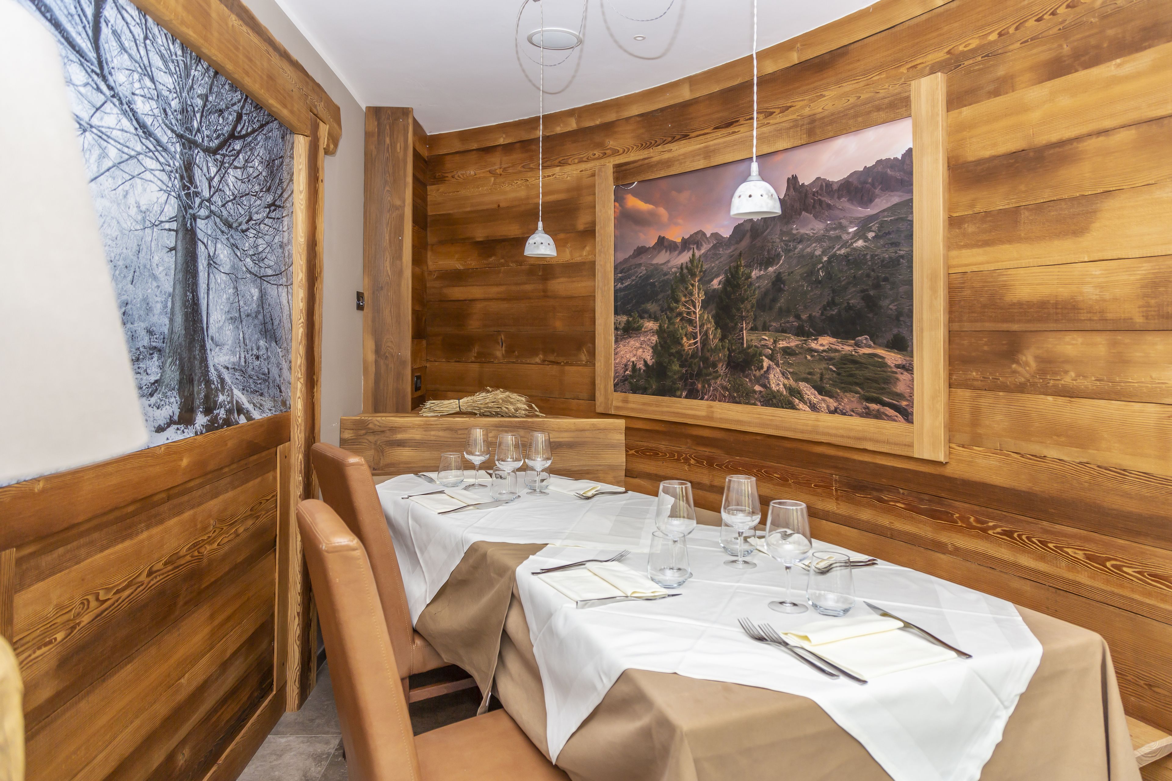 A wooden interior with a dining table set for four, white tablecloths, and two pendant lights.
