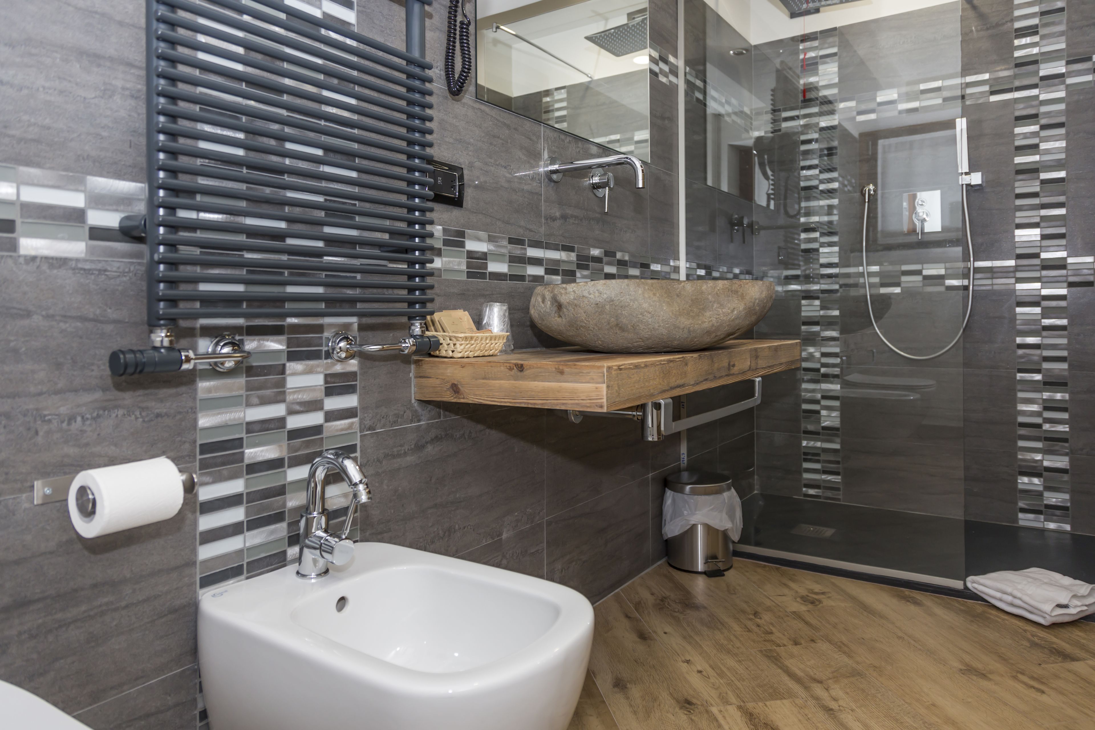 A modern bathroom with a bidet, a wooden vanity, a glass shower enclosure, and a tiled backsplash.