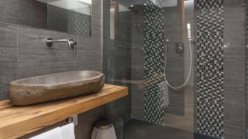 Ein modernes Badezimmer mit Steinwaschbecken, Holzablage und einer Duschkabine mit Mosaikfliesen.